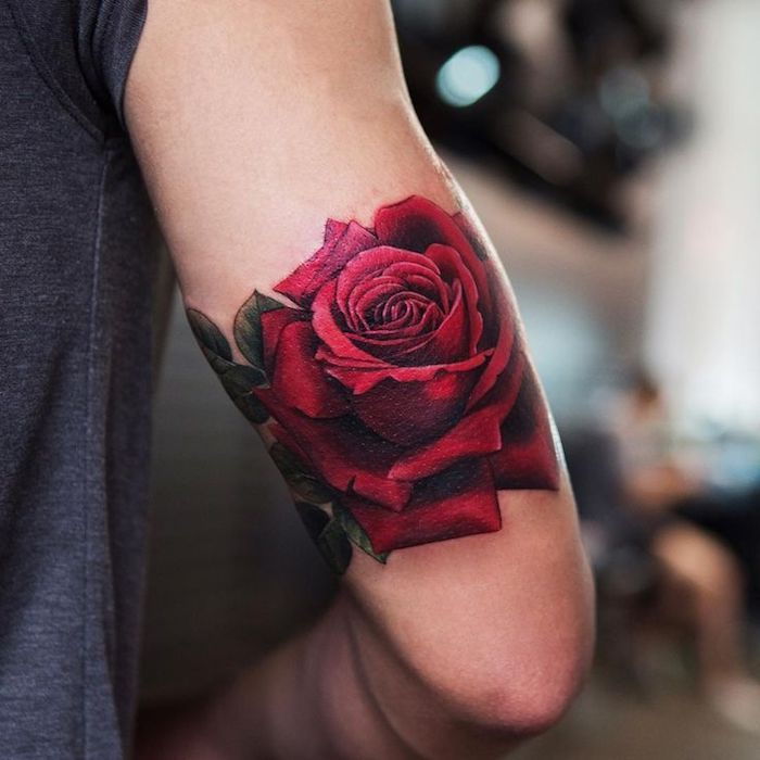 Man med färgad blommatatuering, stor röd ros på sin övre arm