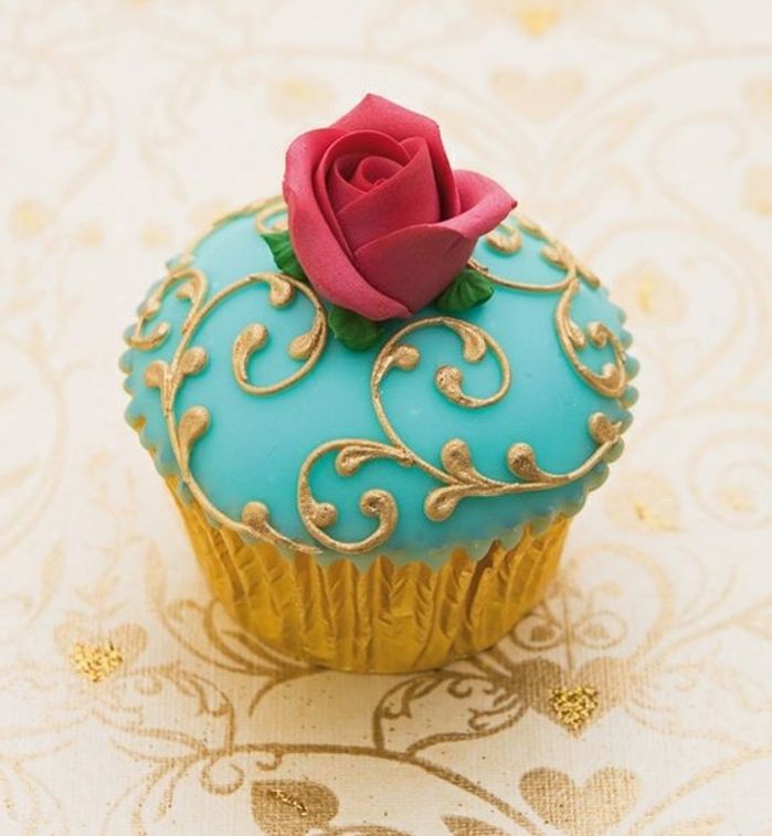 muffin s modrým fondantom so zlatými prvkami a červenou ružičkou
