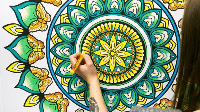 uma menina pinta uma enorme mandala com lápis de cor, borboletas pintar, amarelo, laranja, azul, verde