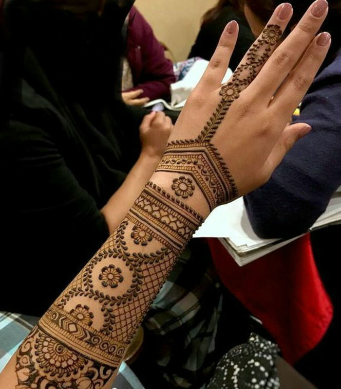 Tatuaże damskie na całej ramieniu i przedramieniu z wieloma małymi ozdobami w kolorze henny, tatuaż na palec serdeczny