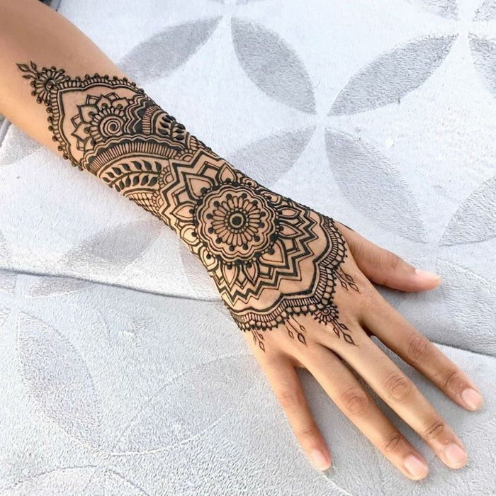 Tatuaggio all'henné in colore nero, tatuaggio al polso e al polso con motivi floreali, donna tatuata