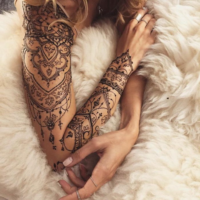 Femeie cu tatuaj frumos în braț, multe elemente mici, accente florale, pătură albă, inele