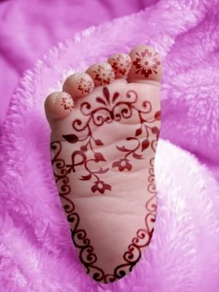 en bebisfot med tatuering i rött hennafärg, tåktatuering för spädbarn, blommotiv, rosa plush filt
