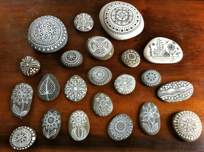 slikanje belih in sivih kamnov z risbami mandala, velikimi in majhnimi kamni, leseno mizo