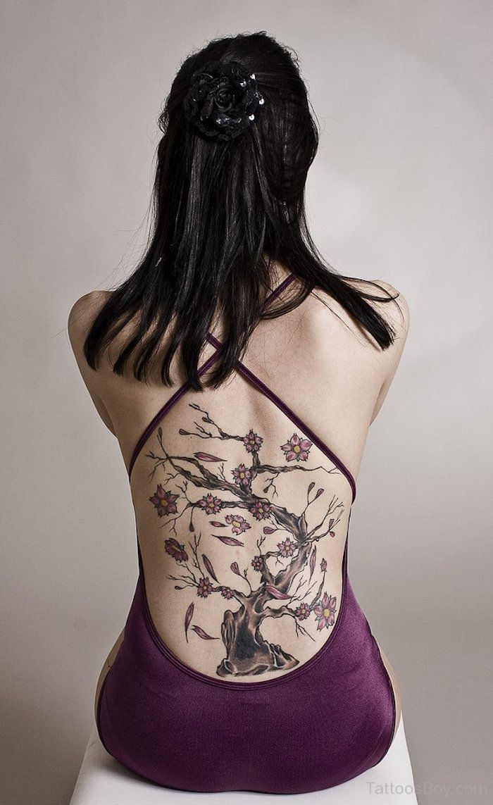 Femeie cu părul negru drept, rochie violet și tatuaj de floare de cireșe pe spate