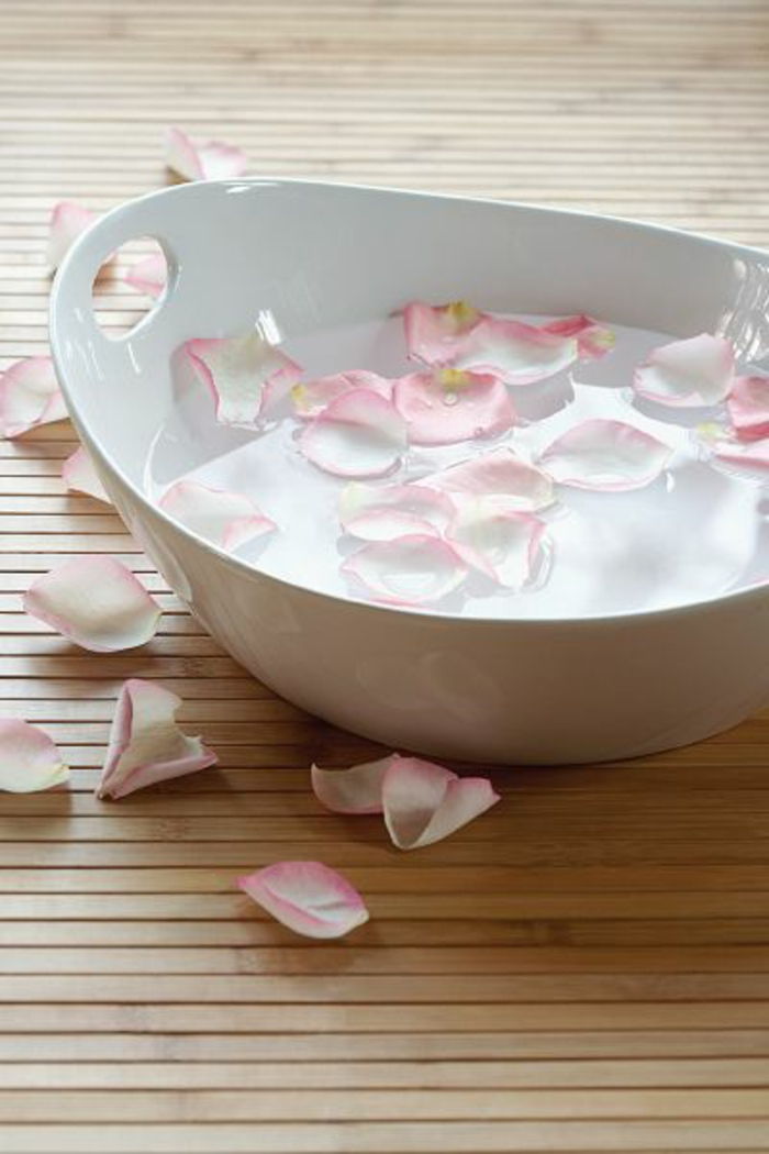 en vit skål med kallt vatten och ljusrosa rosenblad för anti-rynketerapi och små porer
