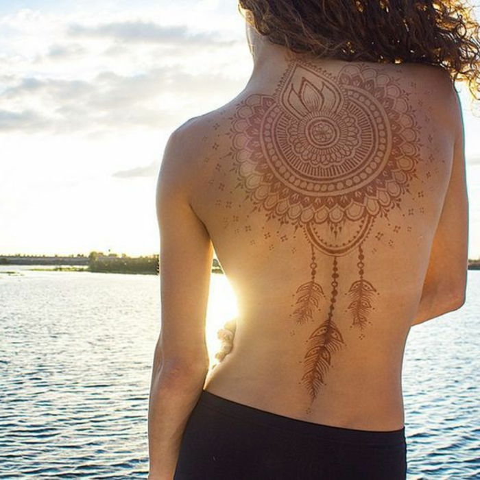 una donna sulla spiaggia con il tatuaggio temporaneo del collettore di sogno di henné in colore rosso, tatuaggio piuma, capelli lunghi ricci