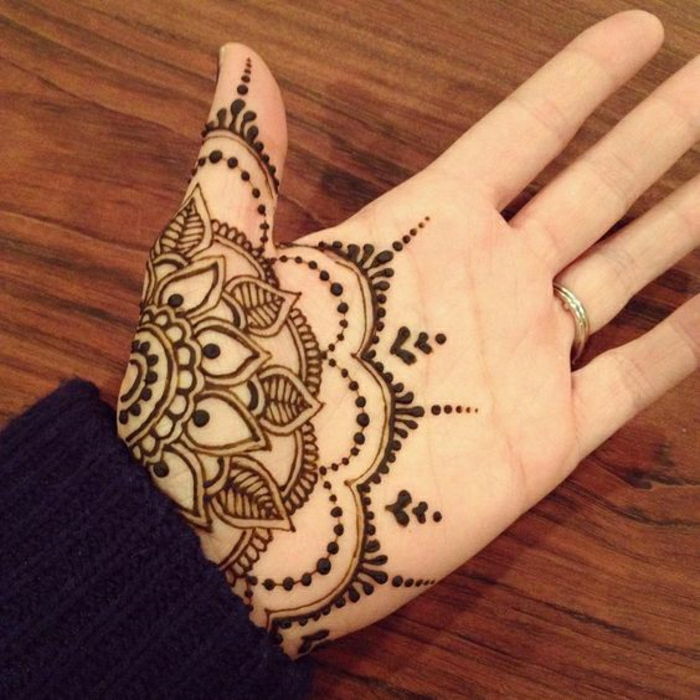 un tatuaj schwaz-roșcat cu henna pe partea interioară a mâinii, mână cu inel de nuntă