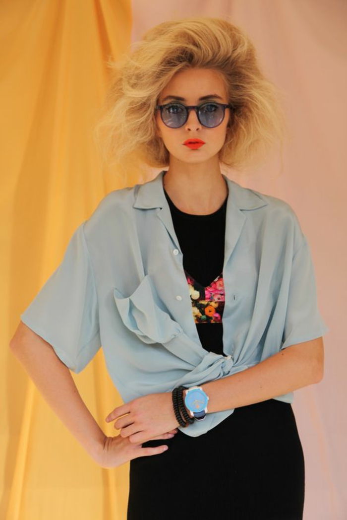 Roupa dos anos 80 para as mulheres com a camisa desproporcionada na luz - t-shirt azul e preto com impressão, óculos de sol enormes, batom néon