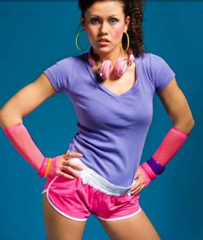 Femeie din anii 80 în îmbrăcăminte sportivă, pantaloni neonpinke scurți, tricou purpuriu, brățări din plastic, mănuși de plasă