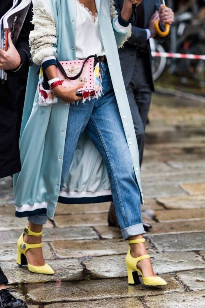 Mulher nos anos 80 com um casaco de bombardeiro, jeans, sapatos amarelos com salto, bolsa rosa com aplicações