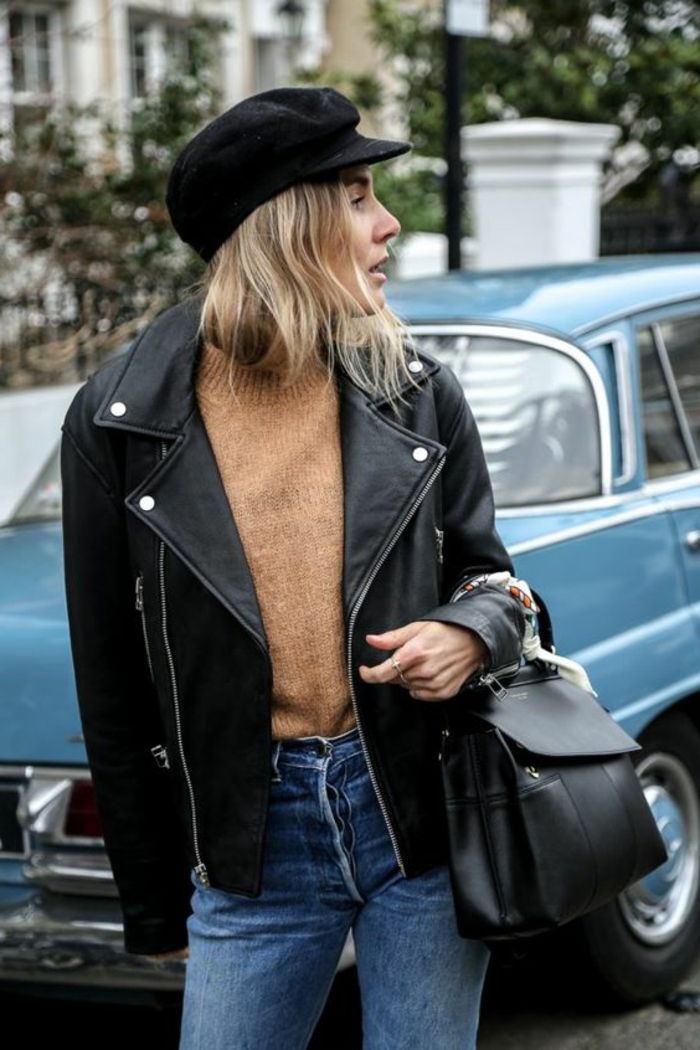 80s look - Femeie cu jacheta de piele in negru, pulover maro, blugi spalati si capac negru de varf