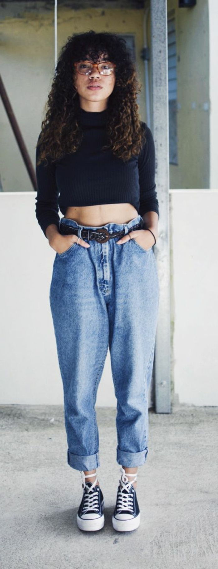 uma garota de roupa dos anos 80 - suéter preto curto, jeans de cintura alta, tênis preto, cabelo encaracolado com franja