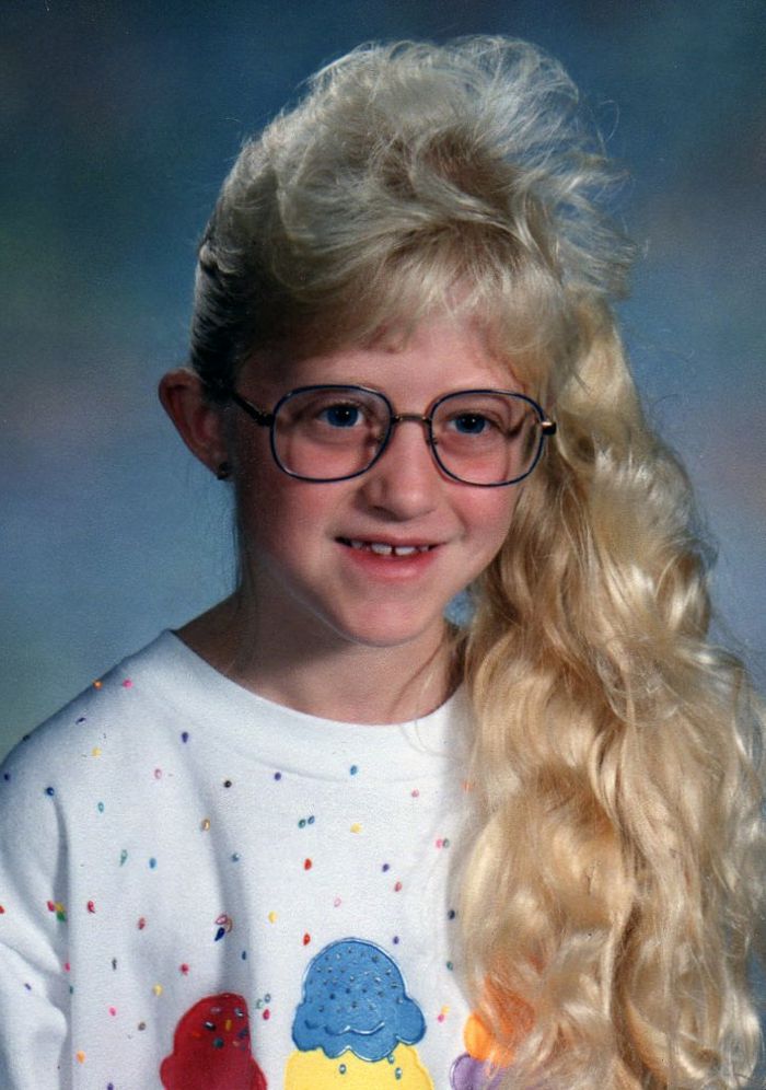 80-talsflicka med sidhästsvans, långt blont vågigt hår, vit blus med tryck, stora läsglasögon