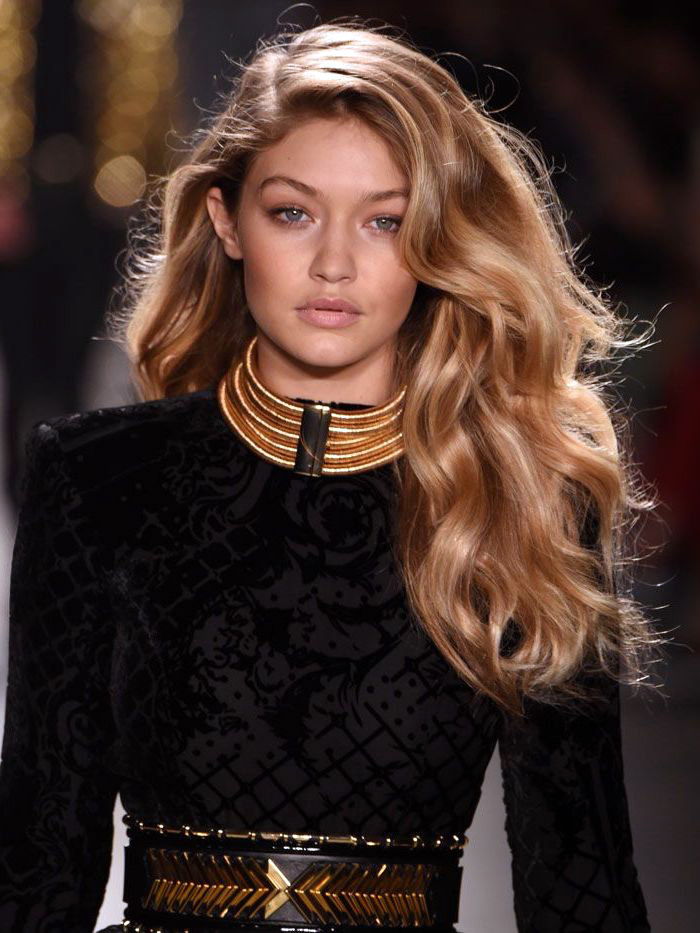 păr lung, cu păr lung, în caramel blond, rochie neagră în combinație cu colier de aur și centură