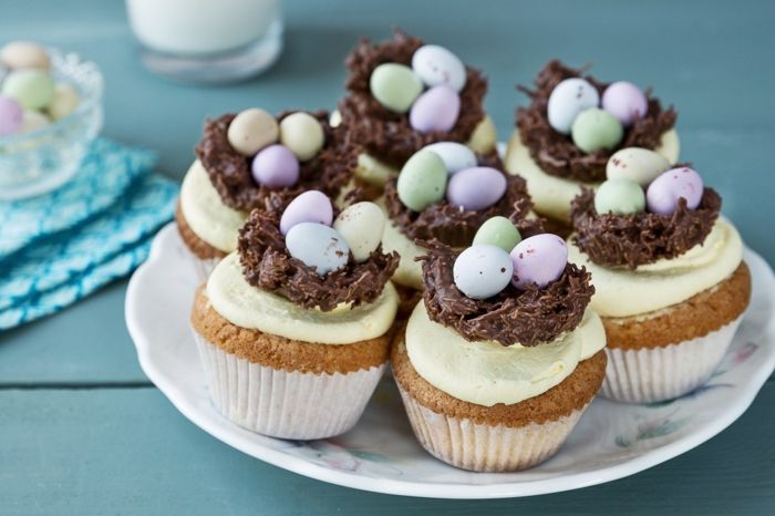 Påske cupcakes med gul glasur og fargerike egg i nest av sjokolade