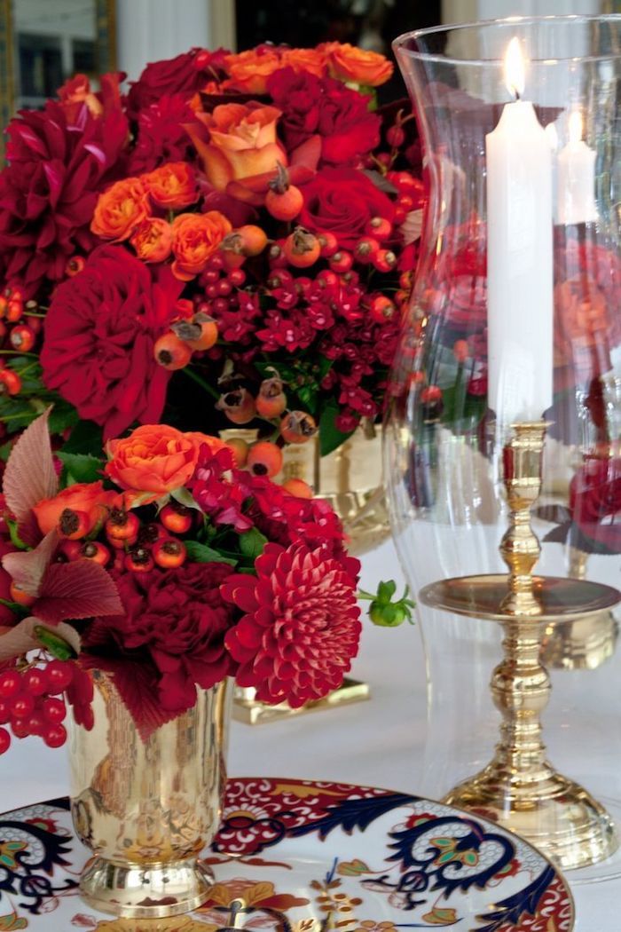 ett ljus i högt glas, två jularrangemang i guldvaser full av röda blommor