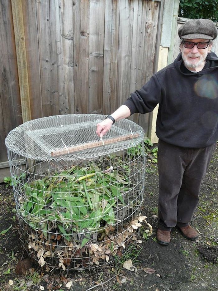 Hier vindt u een foto met een oude man met een bril en zijn zelfgemaakte composter met groene bladeren