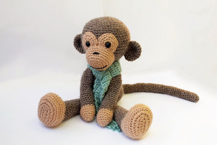 urocza małpka w brązowym kolorze z zielonym szalikiem - wzór szydełkowy Amigurumi