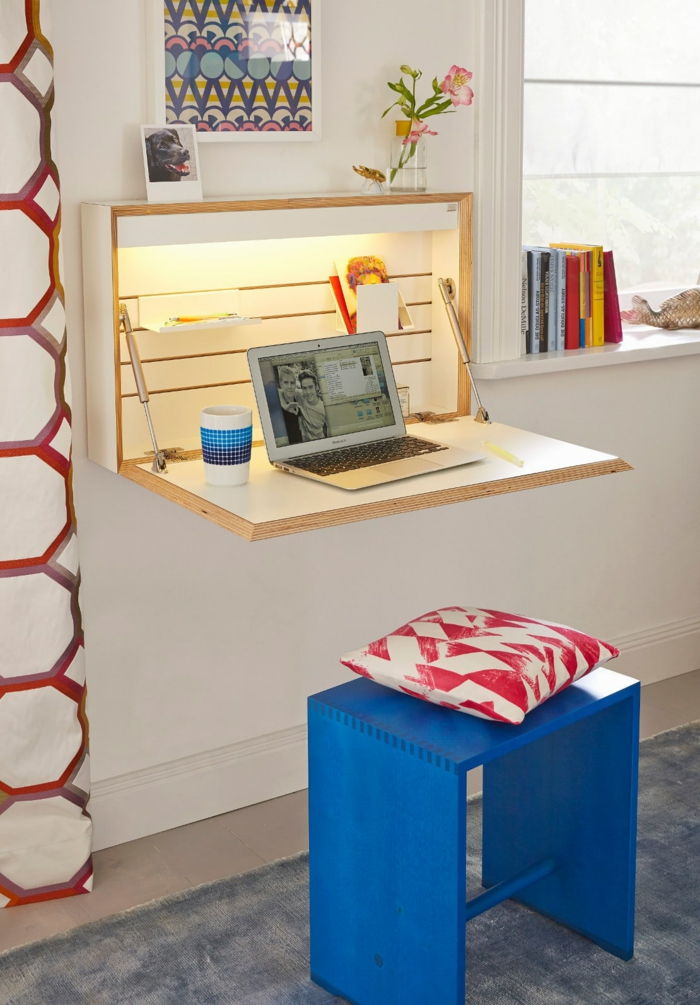 Birou pentru spații mici, idei funcționale și practice, scaun albastru din lemn, pernă alb-roșie, cărți pe fereastră, laptop și cupă de porțelan pe masă