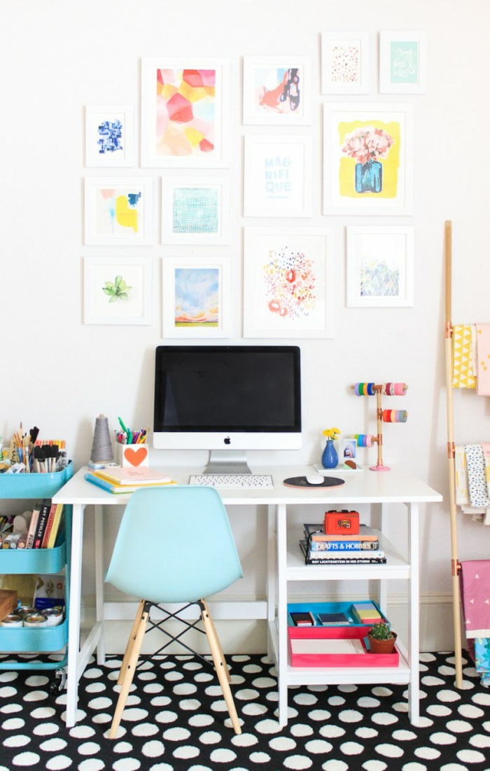 Mobilier de studiu, multe picturi pe perete, covor negru cu puncte albe, birou alb și scaun albastru