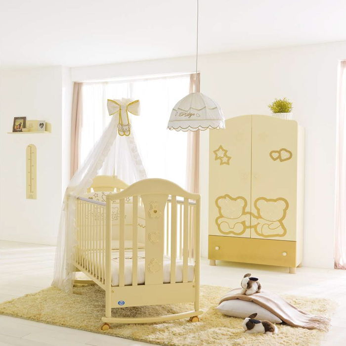 Įrengtas kūdikio kambarys, geltoni baldai ir baltos sienos, vaikiška lovelė su danga ir ritinėliai, gražus ir praktiškas