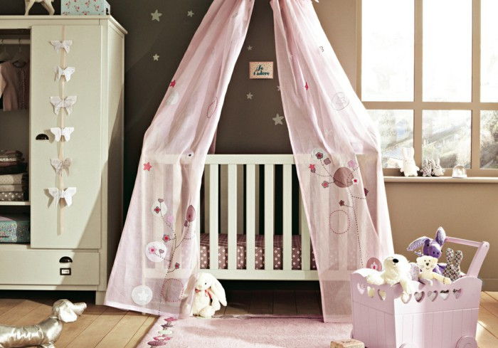 Kūdikių kambarys merginoms pastelinėmis atspalvėmis, maži įdaryti gyvūnai, kūdikių lovelė su dangaus rožinės spalvos