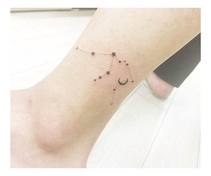 svart stjerne tattoo - et bein med en liten svart tatovering med et stjernebilde med små svarte stjerner og en svartmåne