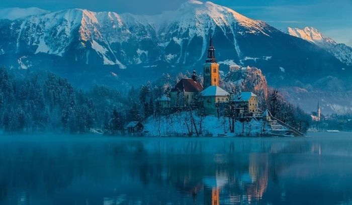 imagini frumoase de iarnă - lac și o insulă cu o biserică și case mici - munți de iarnă cu zăpadă și o pădure cu copaci și. zăpadă