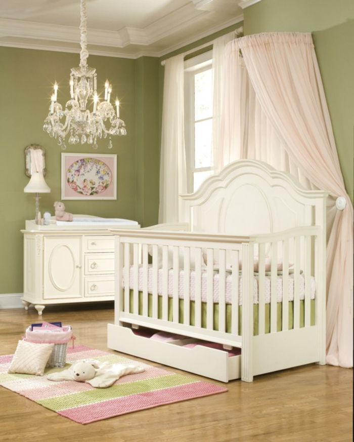 stilingas kūdikio kambarys, žalios sienos, balti mediniai baldai, žaisminga liustra, lovelė su šviesiai rausva danga