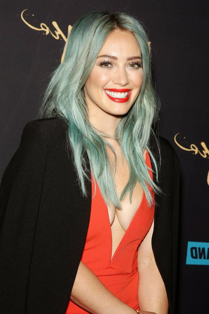 Hilary Duff com cabelo azul brilhante, lábios vermelhos brilhantes, Pozellanteint, grande korallfarbenes Outfit- vestido e blazer preto