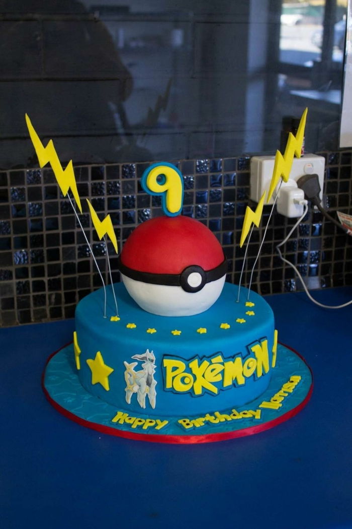 una grande torta pokemon blu con pokeball rosso e due lampi gialli e stelle gialle e un'intestazione gialla