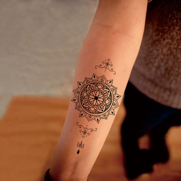 jovem mulher com tatuagem de mandala no antebraço, pequena tatuagem no braço inferior com motivos de mandala, pequenos símbolos tribais em preto