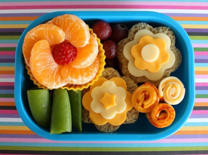 två smörbröd i form av blommor, gula och vita ostar, färsk frukt, färgglad bordsduk med ränder i alla färger