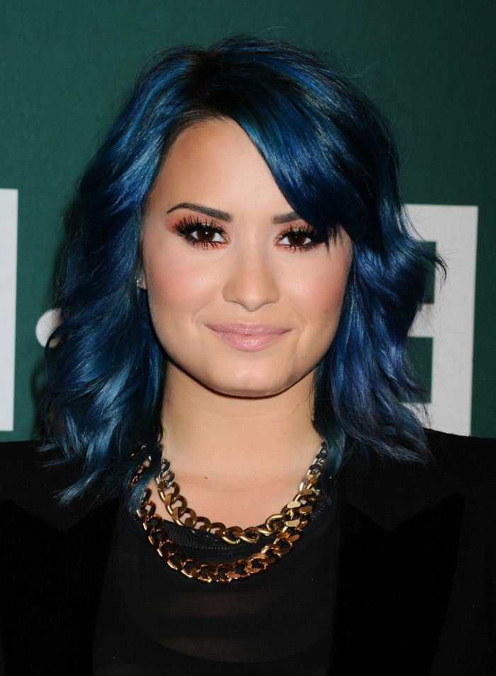 Demi Lovato com cabelo azul, lábios sem brilho, pêssego vermelho e sombra nos olhos, corrente de ouro
