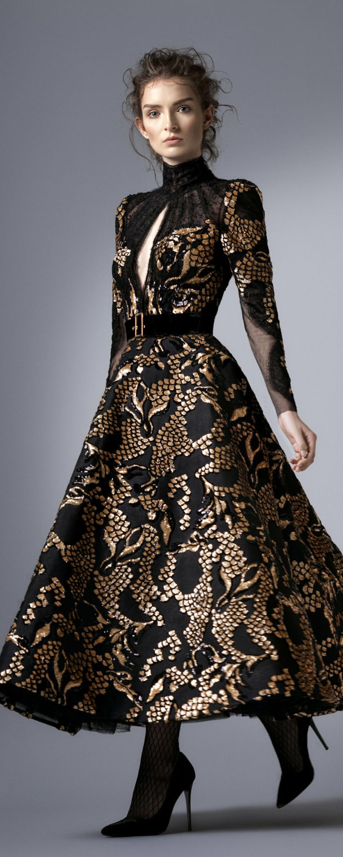 Elegantné dámske módy - dlhé šaty v čiernej a zlatej farbe so zlatou Semtgürtel s uzatváracím Pollokragen a otvorená na hrudi, priepustné Hochsteckfrisur pre kučeravé vlasy, sieťované pančuchy a čierne topánky na podpätku