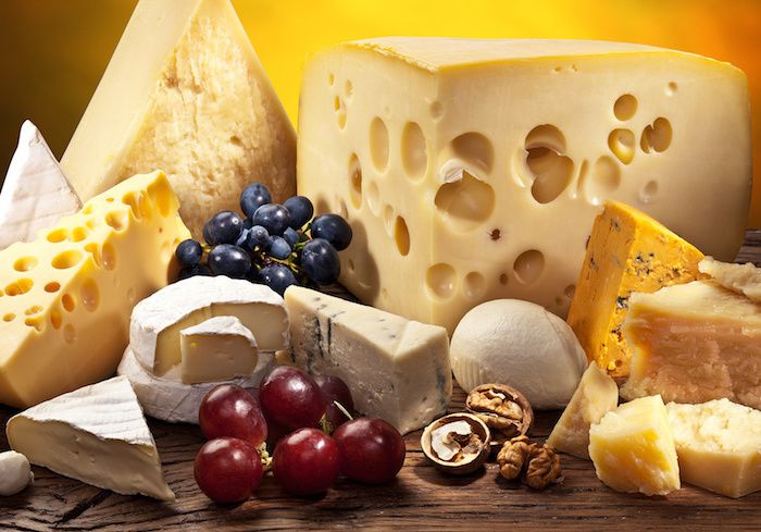 olika typer av ost med och utan hål, ostar med stora leenden, två typer av blå ost med olika färger, två sorter av röda druvor, massivt träbord och gul bakgrund