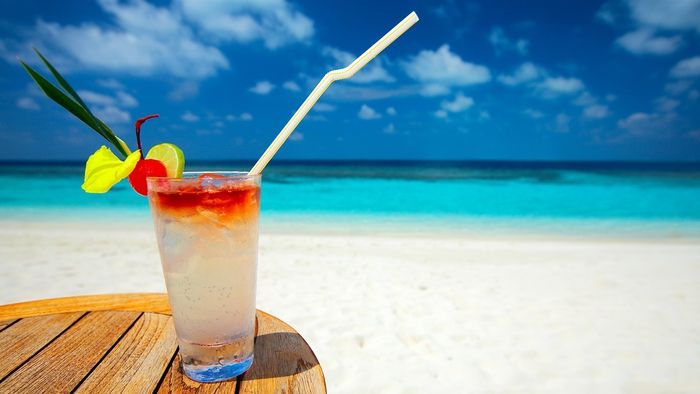Cocktail med sitrusfrukter, havet som bakgrunn, en forfriskende drink og nyt solen
