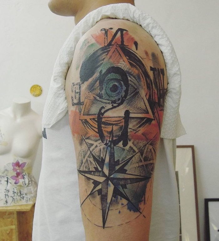 Człowiek z szalonym, kolorowym tatuażem na ramieniu z dużym niebieskim okiem i dużym czarnym kompasem