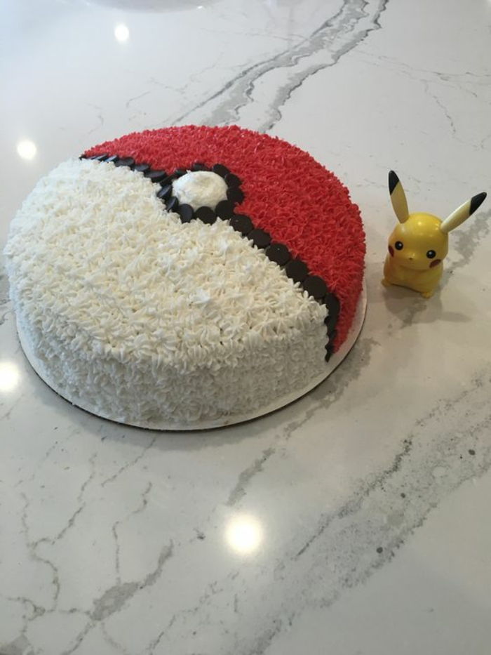 Deliciosa torta de pokemon que parece em pokebola - com creme preto, branco e vermelho, e um pequeno pikachu amarelo
