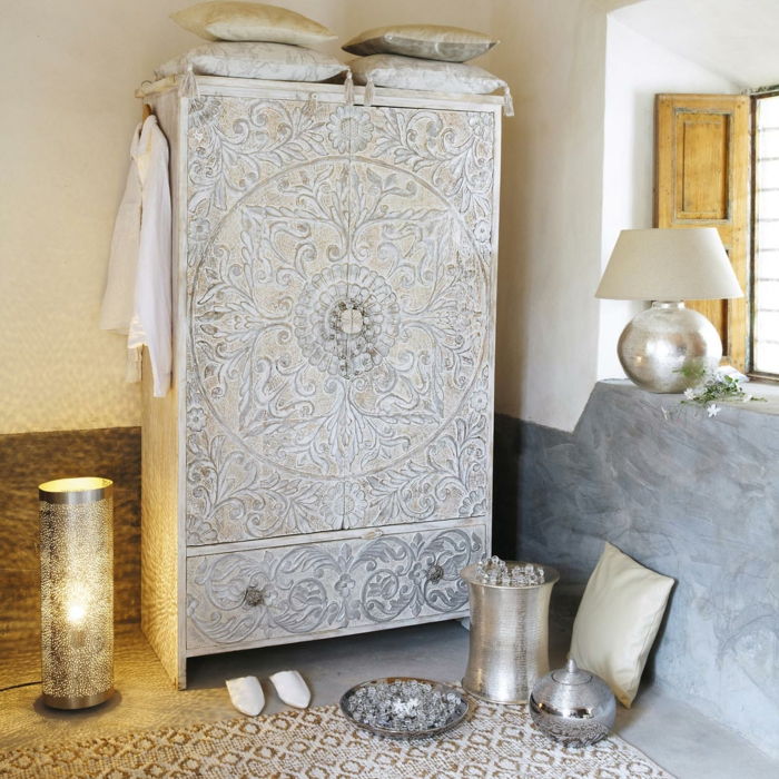 okrasna dekorativna omara z orientalsko dekoracijo, obarvana z belo kovinsko deko ploščo, lahko svečo in svetilko zamisli