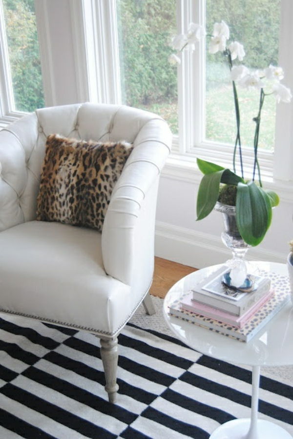 Obývacia izba s bielym kreslom, bielymi kvetmi, vankúšmi a oknom