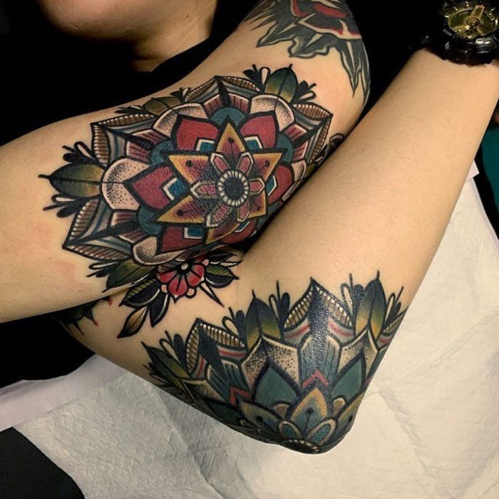 Donna in uno studio di tatuaggi con tre tatuaggi colorati: una spalla, un braccio superiore e un tatuaggio a gomito, indossa un orologio nero con quadrante placcato in oro