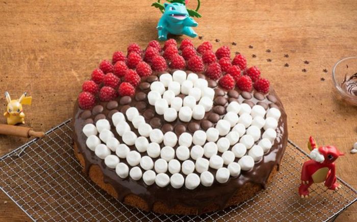 Uma grande torta de pokemon de chocolate com bombons brancos e framboesas vermelhas e três pequenos seres pokemon e pikachu