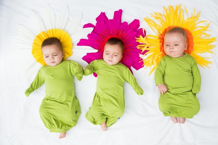 Tri luštna otroka oblečena v cvetje, zelena oblačila in blazine, kot rože v rumeni in vijolični barvi