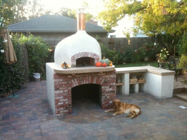 Câinele se află lângă un cuptor de pizza din piatră și cărămidă în grădină