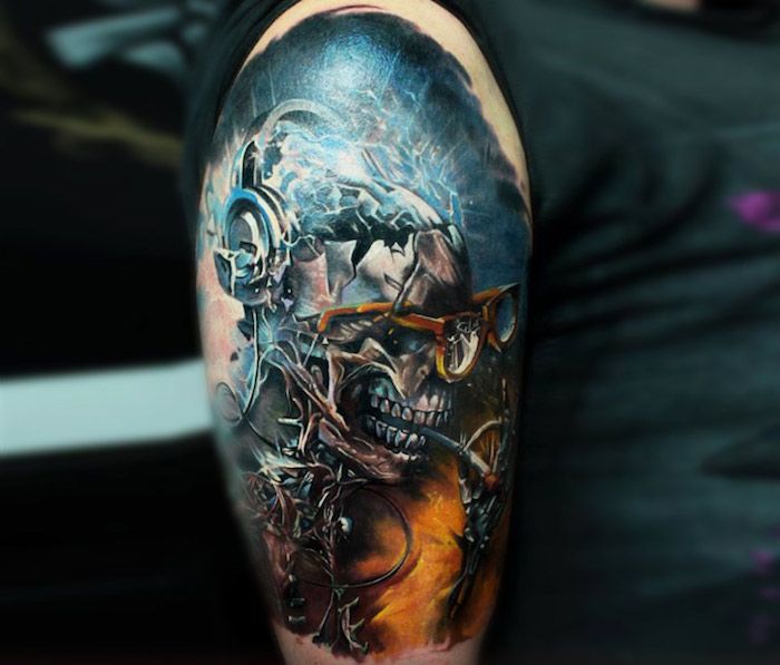O mână cu un tatuaj albastru colorat, cu un craniu metalic și ochelari și o țigară