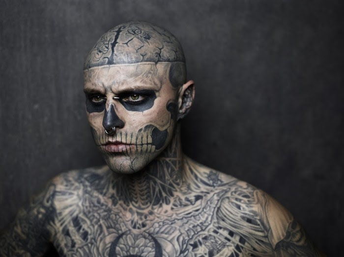 en tatovert beskjeden mann med mange tatoveringer og en tatovering med en stor, hvit hodeskalle med hvite tenner og to svarte øyne