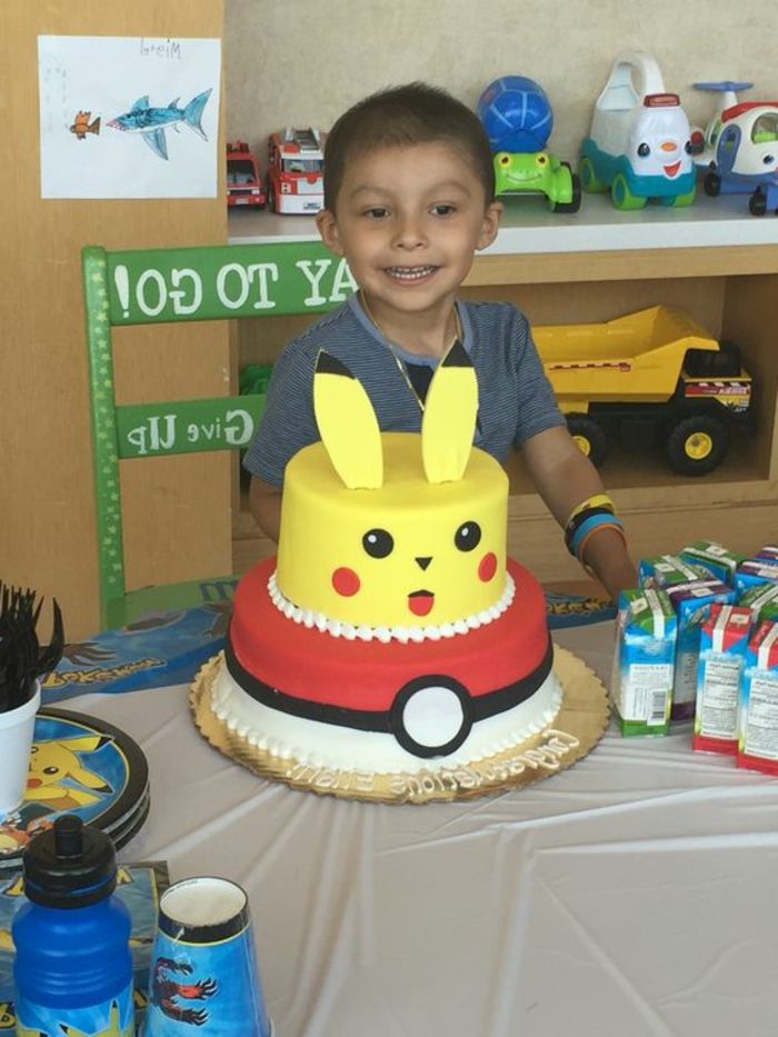 ecco un ragazzino con una torta a due piani - un pokemon giallo che è pikachu e una pokeball rossa