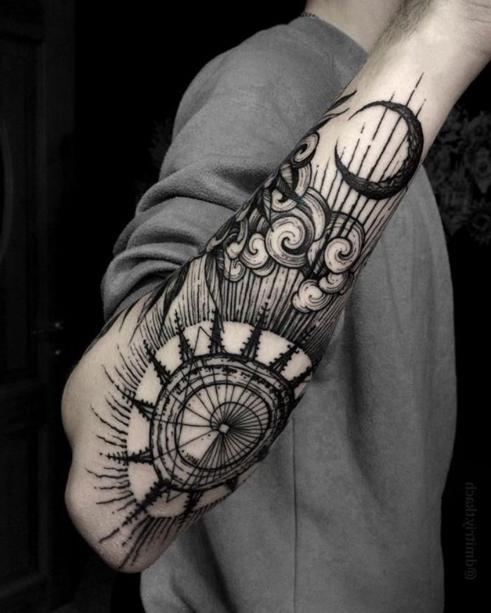 oto pomysł na czarny tatuaż kompasu na ręce mężczyzny - z kompasem, chmurami i czarnym księżycem